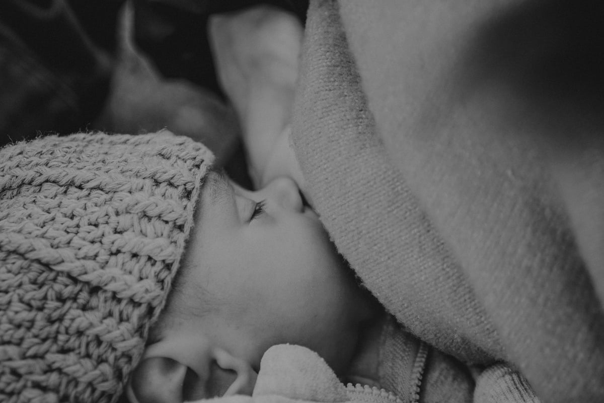 a black and white photo of a baby wearing a knitted and breastfeeding