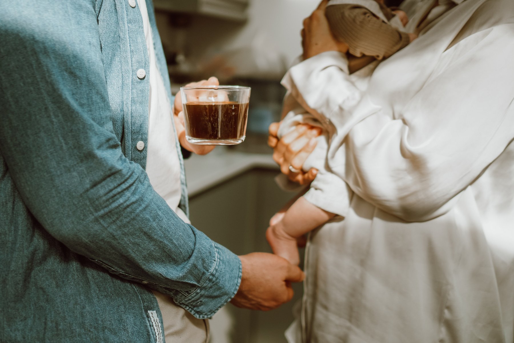 a person holding a cup of coffee in front of another person and a baby