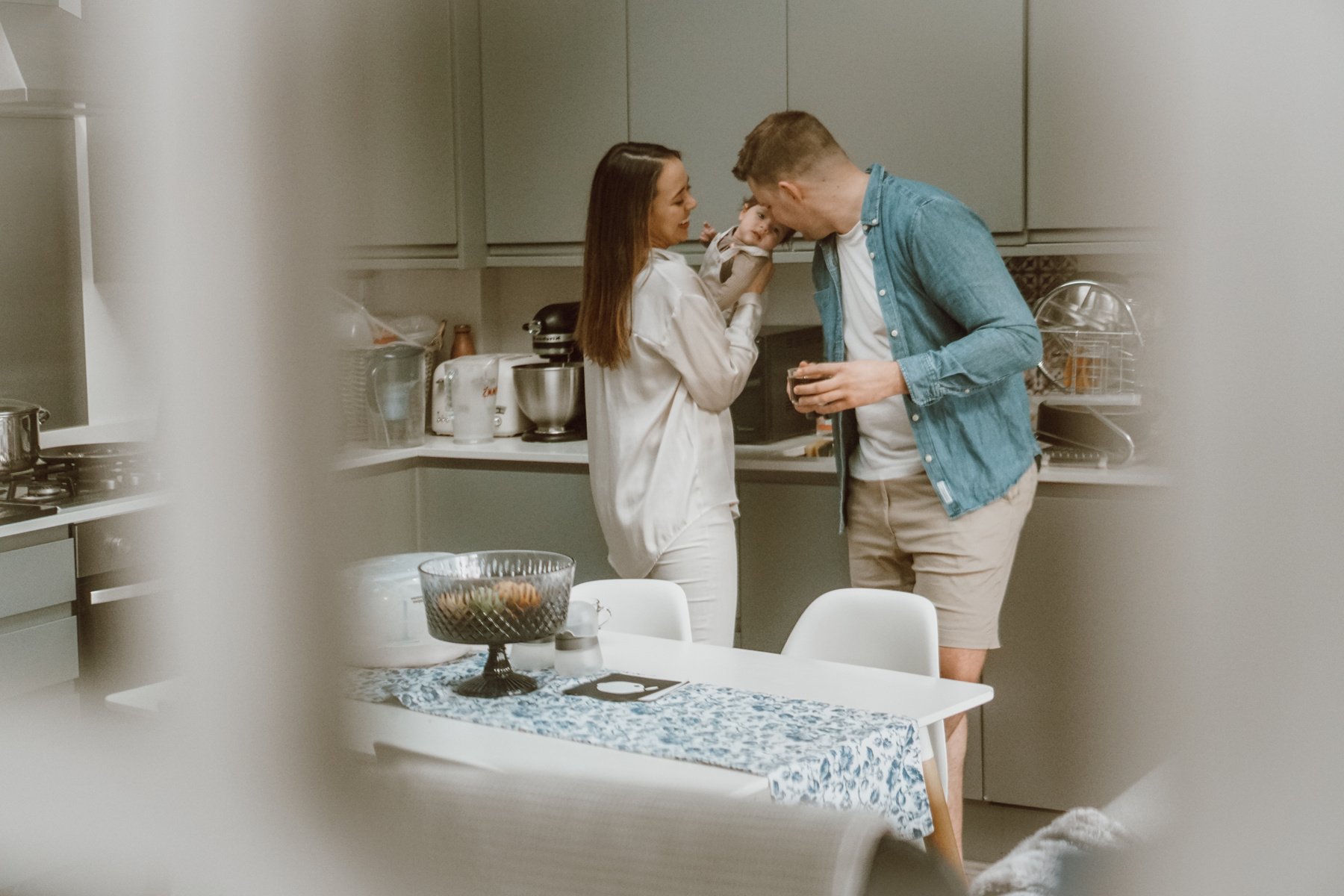 a mum and dad are standing in a kitchen with their newborn baby