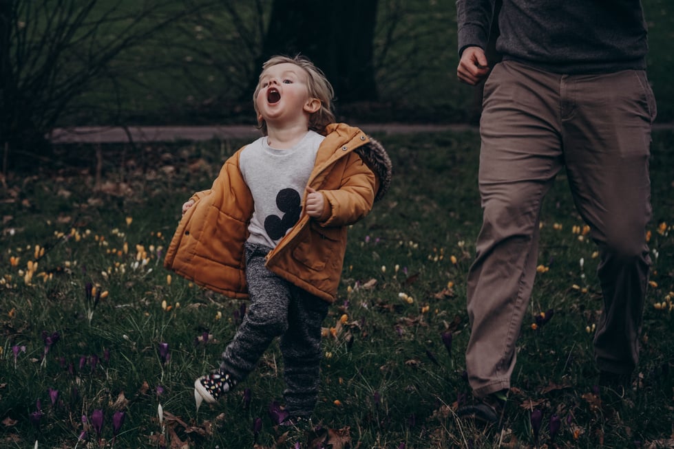 a little boy running in the park with his father