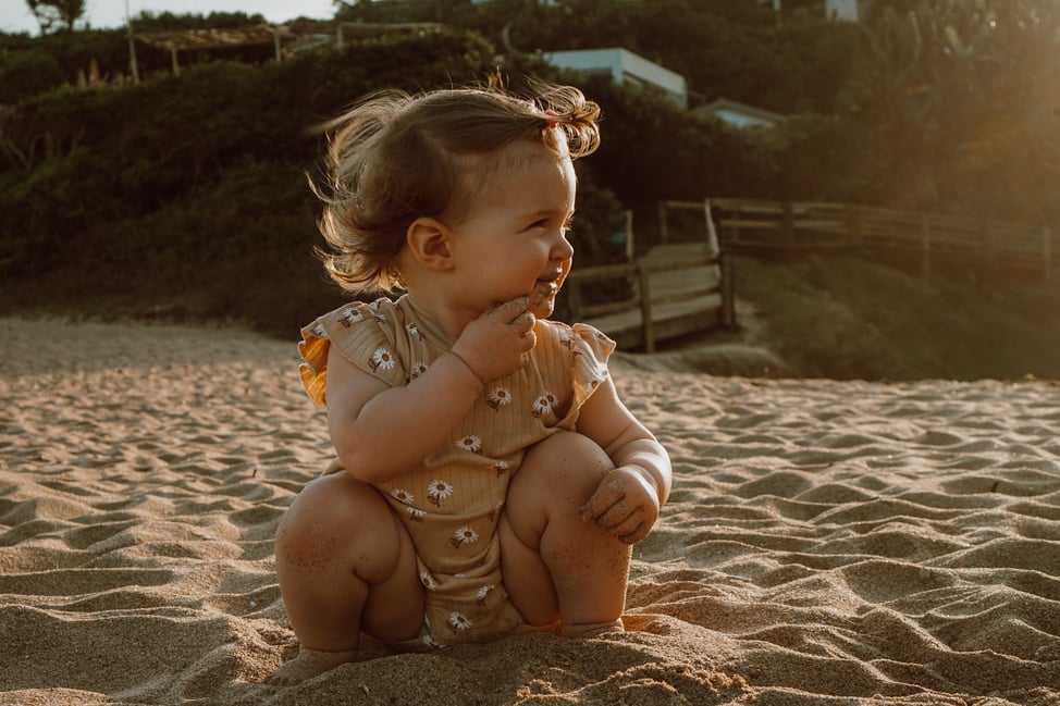 a baby sitting on the beach at sunset